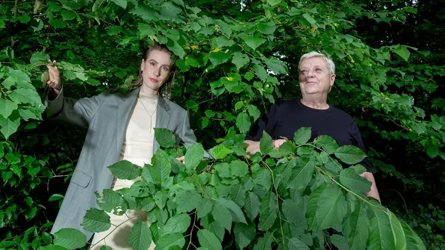 Roos en Barbara staan tussen de groene bladeren. Roos (links) draagt een grijze oversized blazer, Barbara (rechts) een zwart t-shirt.