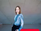 Laura Stek, een witte vrouw met lichtbruin haar, blauwe ogen en blauw shirt met lange mouwen, staat voor een betonnen muur en kijkt in de camera.
