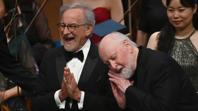 Een lachende regisseur Steven Spielberg, gekleed in een zwarte smoking en componist John Williams met zijn hoofd op Spielbergs schouders