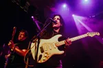 Band Ribbon Skirt: frontvrouw met een gitaar aan het zingen en op de achtergrond de gitarist