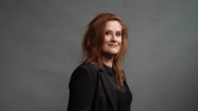 Lotje IJzermans poseert staand in een zwarte outfit voor een grijze achtergrond, met een rustige glimlach en haar hand in haar zak.