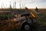 Een verwoeste auto en een militair op de rug aan de rand van een bos.