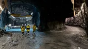 Drie mensen in werkkleding lopen door een ondergrondse tunnel.